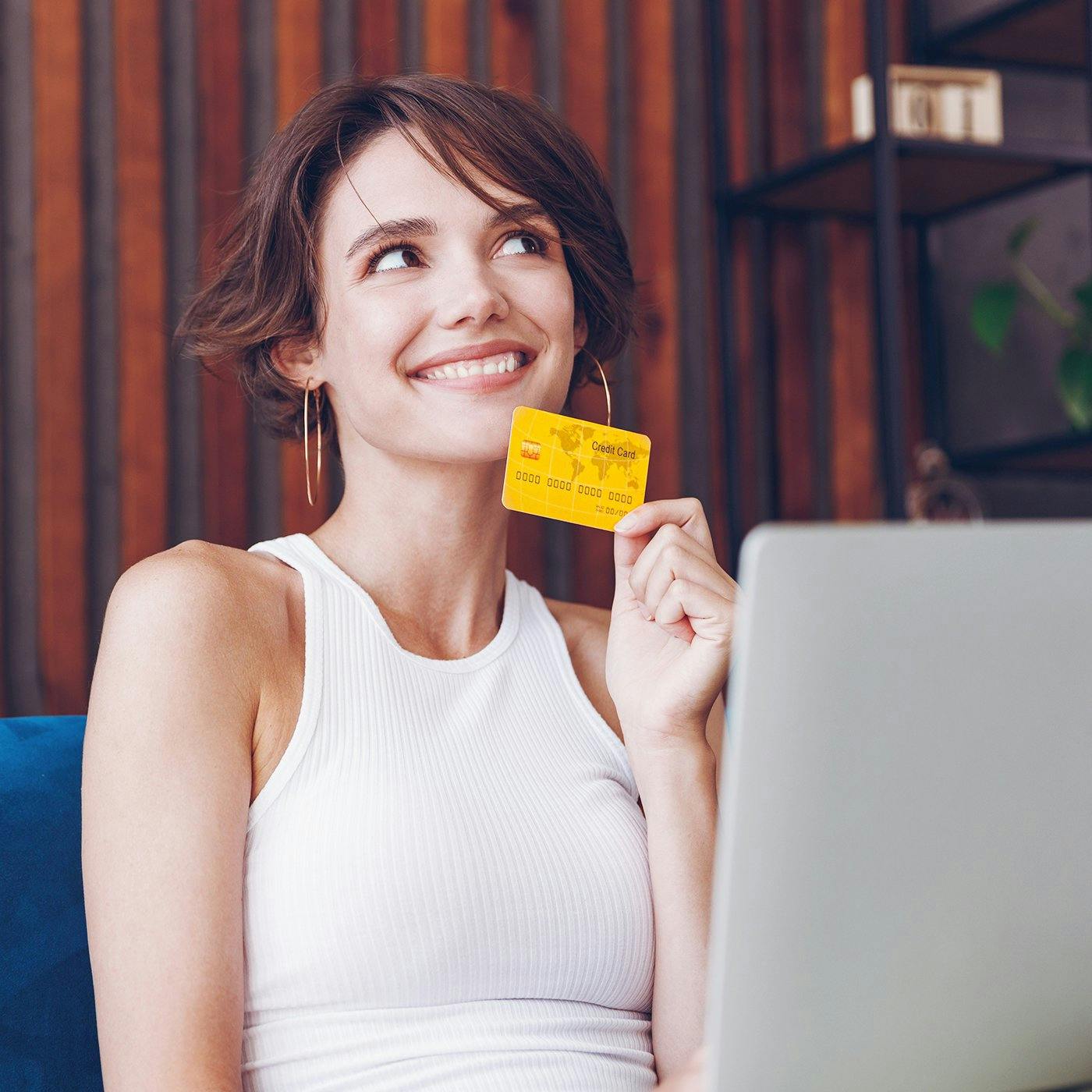 A smiling woman thinking while holding a credit card