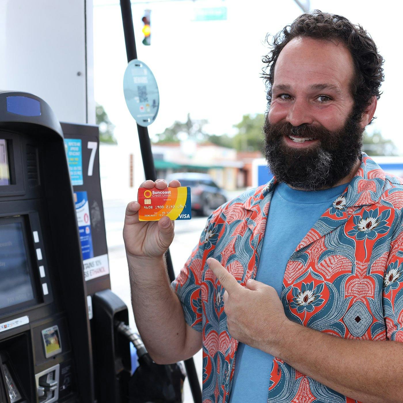 A smiling man holding a Suncoast credit card at a gas station